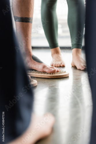 cropped view of man with tattoo on legs standing on nail board near people in yoga studio.