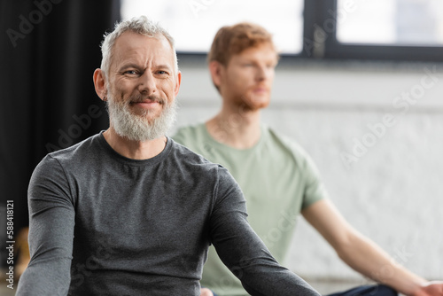 Bearded middle aged man smiling at camera in yoga studio.