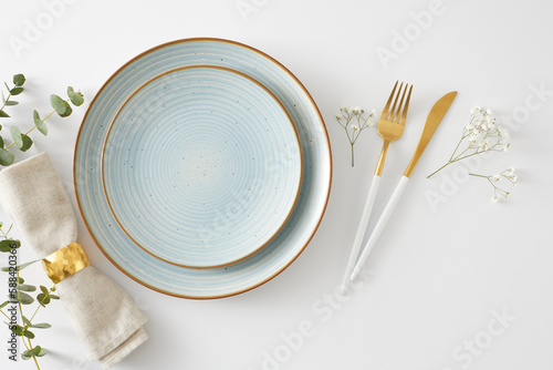 Table setting concept. Top view photo of empty plate cutlery knife fork fabric napkin with gold ring and eucalyptus leaves with gypsophila flowers on white background
