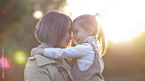 An adorable, sweet little girl hugs her young mother during a walk in a spring park.