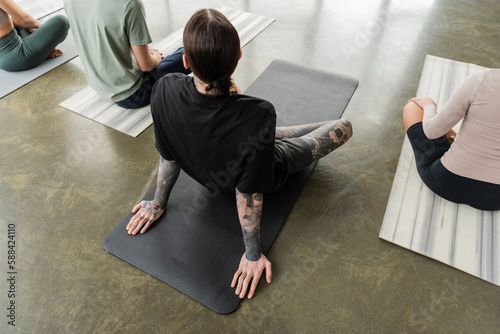 Overhead view of tattooed man sitting on mat near interracial people in yoga class.