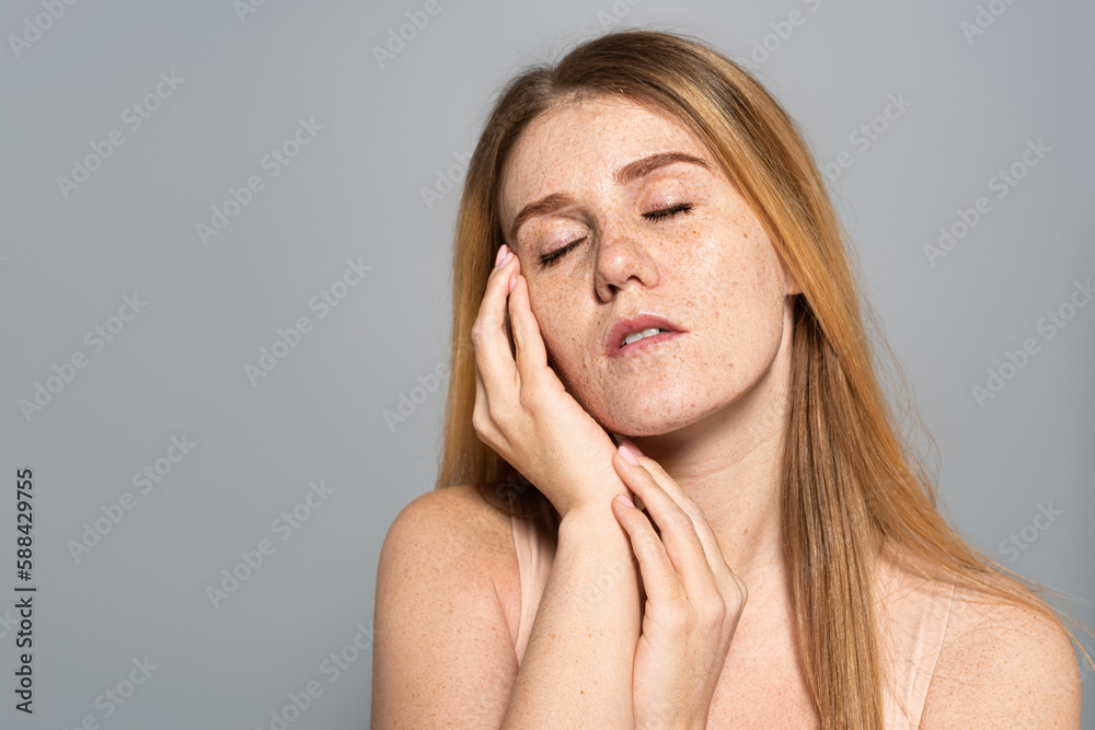 Young freckled woman touching face isolated on grey. Young freckled woman touching face isolated on grey.