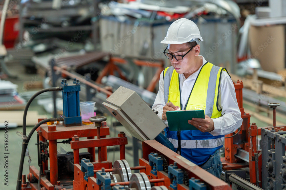 Asian male engineer in uniform inspection warehouse and check control heavy machine construction installation in industrial factory. technician worker check for repair maintenance operation system Asian male engineer in uniform inspection warehouse and check control heavy machine construction installation in industrial factory. technician worker check for repair maintenance operation system