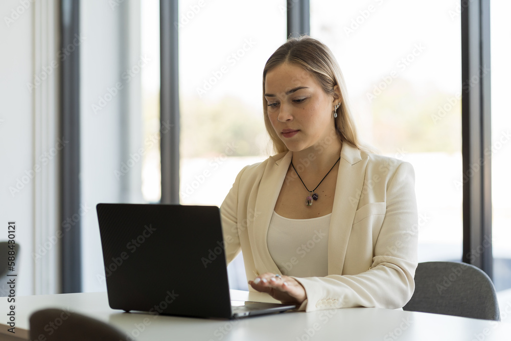 Young business woman working in modern office, wearing suit and typing on laptop computer on office table