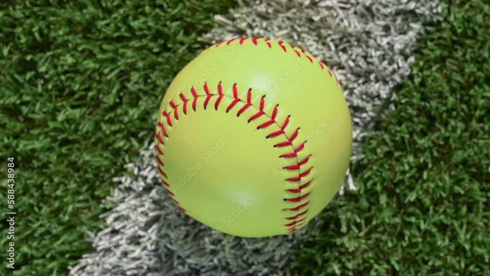 An overhead closeup shot of a softball sitting on the foul line of the outfield grass as the