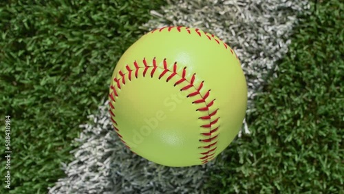 An overhead close-up shot of a softball sitting on the foul line of the outfield grass as the camera rotates – slow. photo