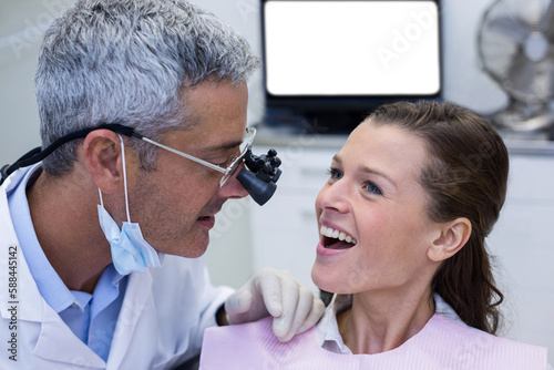 Dentist examining female patient with dental loupes