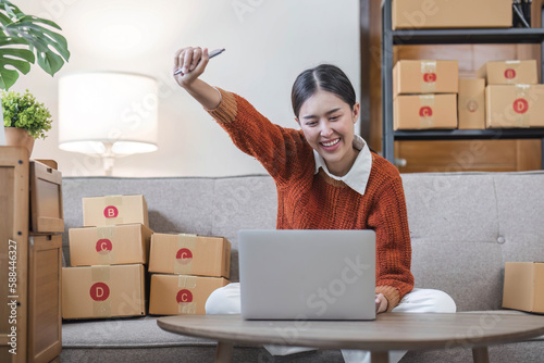 Asian business woman leaning on the sofa use laptop computer checking customer order online shipping boxes at home. Starting Small business entrepreneur SME. Online business, Work at home concept.