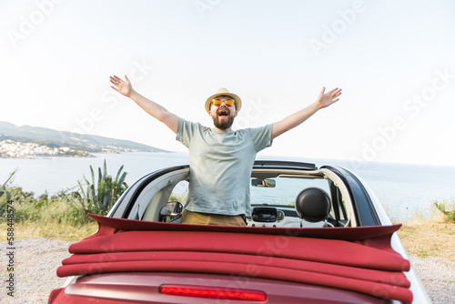 Happy man sitting in white convertible car with beautiful view and having fun - travel summer vacation and rental car concept