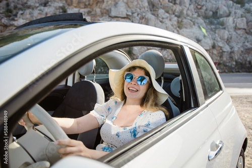 Smiling woman wearing hat and sunglasses enjoying her summer road trip in cabrio car. Freedom and tourism vacation. travel trip and summer holidays © satura_