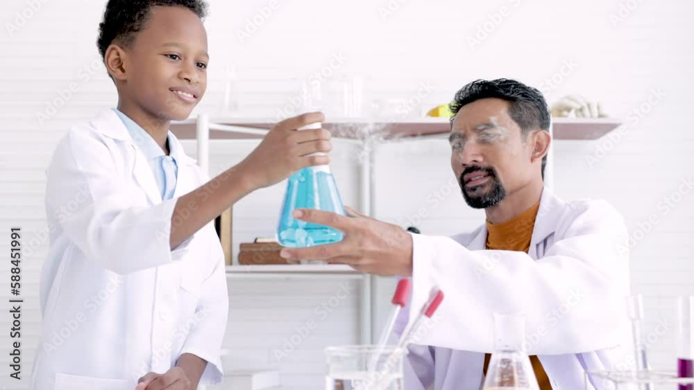 Teacher in white gown and student scientists making experiment in lab, teaching and guiding in his elementary school in science class. Happy african boy learning in chemistry class with professional Teacher in white gown and student scientists making experiment in lab, teaching and guiding in his elementary school in science class. Happy african boy learning in chemistry class with professional