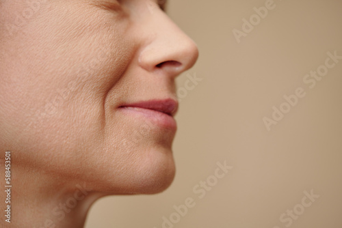 Face of middle-aged woman with nasolabial folds, isolated on beige photo