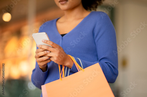 Unrecognizable Black Female Using Phone Holding Shopper Bags At Mall