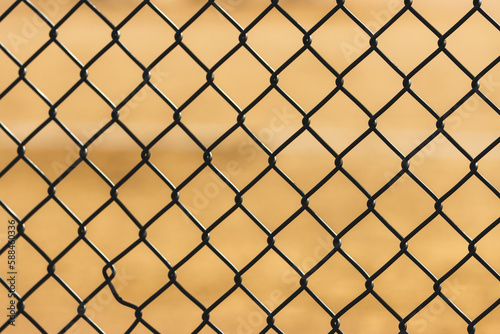 a fence background with a softball/baseball field in background.