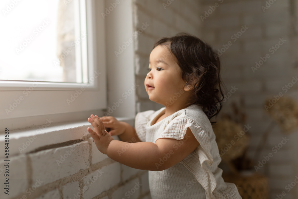 Adorable Asian Baby Girl Looking Out Of Window At Home Adorable Asian Baby Girl Looking Out Of Window At Home