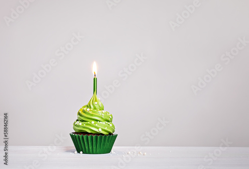 Green cupcake with sprinkles and lit birthday candle on a white grey background.