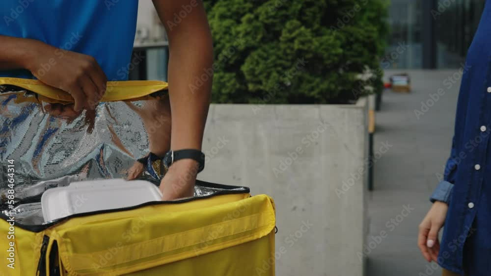 Close up View of the African American Man Delivers Lunch Boxes to Client, Taking Them From the Yellow Backpack. Courier Gives Lunch to an Office Worker. Food Delivery Close up View of the African American Man Delivers Lunch Boxes to Client, Taking Them From the Yellow Backpack. Courier Gives Lunch to an Office Worker. Food Delivery