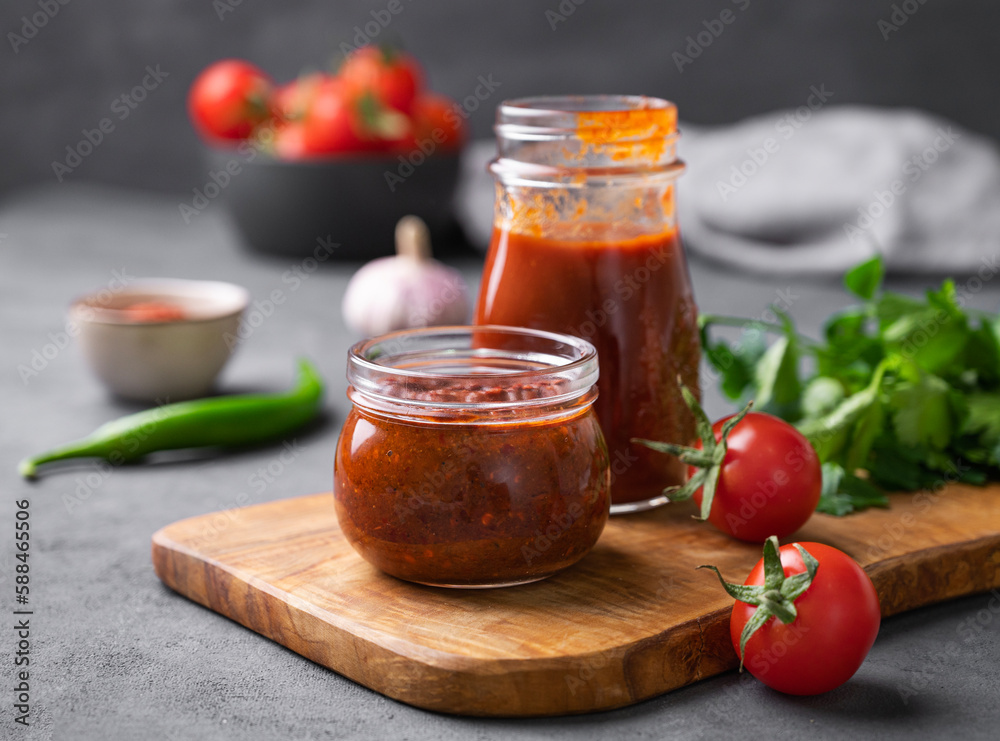 Tomato paste of hot pepper marinara with garlic, tomatoes and herbs in jars on a wooden board on a dark background. Tomato paste of hot pepper marinara with garlic, tomatoes and herbs in jars on a wooden board on a dark background.