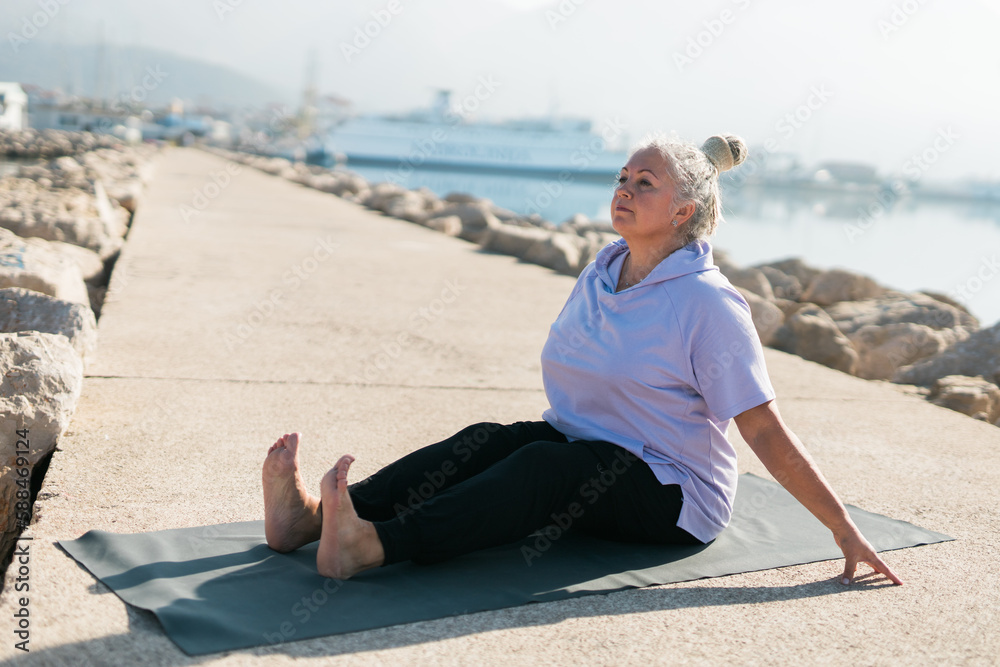 Fototapeta premium Mature old woman with dreadlocks practicing yoga and tai chi outdoors by the sea - wellbeing and wellness