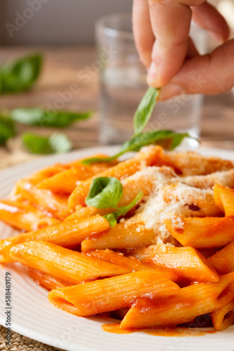 Pasta with tomato sauce, Parmesan cheese and basil, penne pomodoro, a classic Italian dish on a white plate and wooden table.