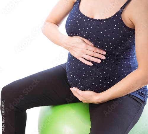 Pregnant woman holding belly while sitting on exercise ball