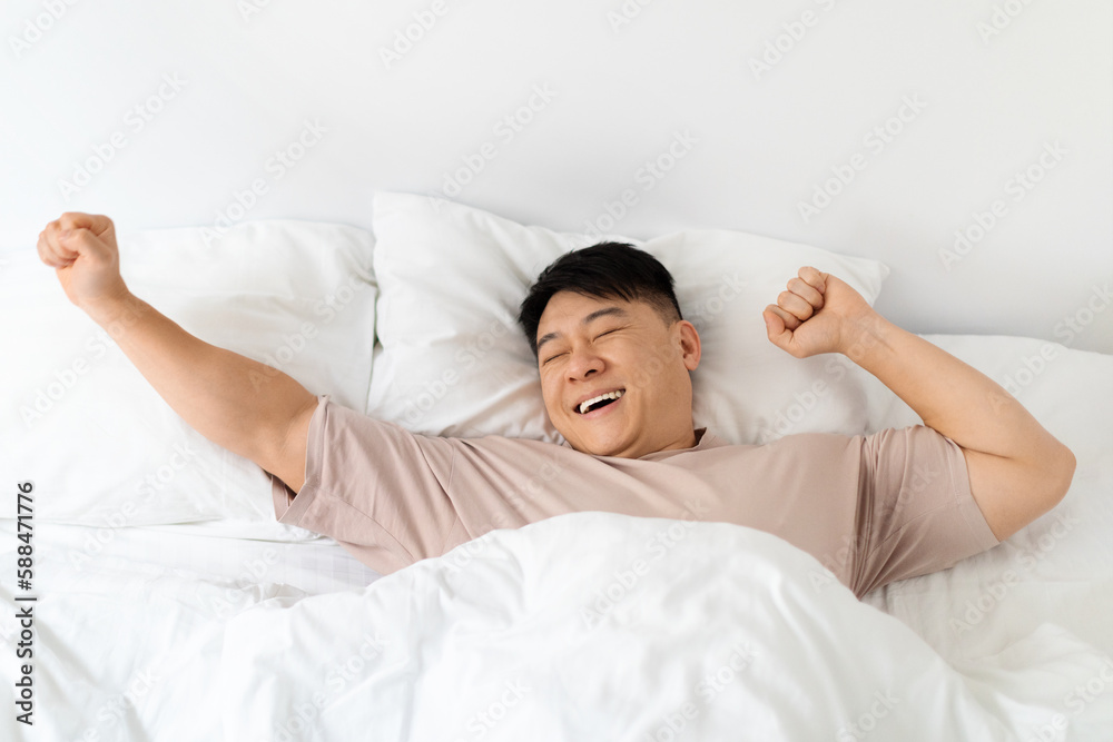 Top view of smiling asian man stretching in bed Top view of smiling asian man stretching in bed