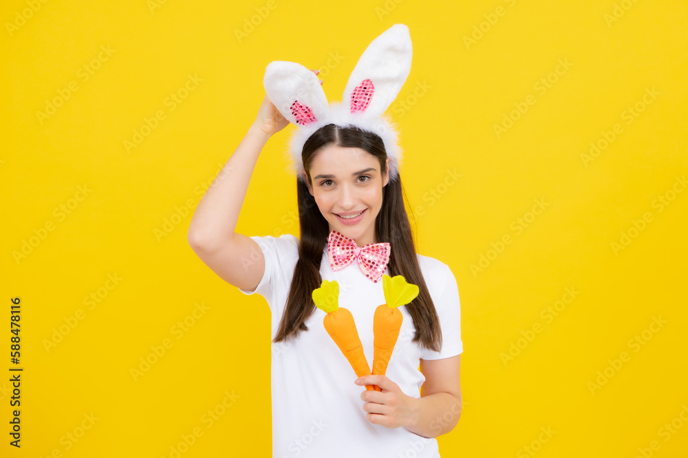 Rabbit girl with toy carrot. Cheerful smiling girl in bunny ears celebrating Easter.