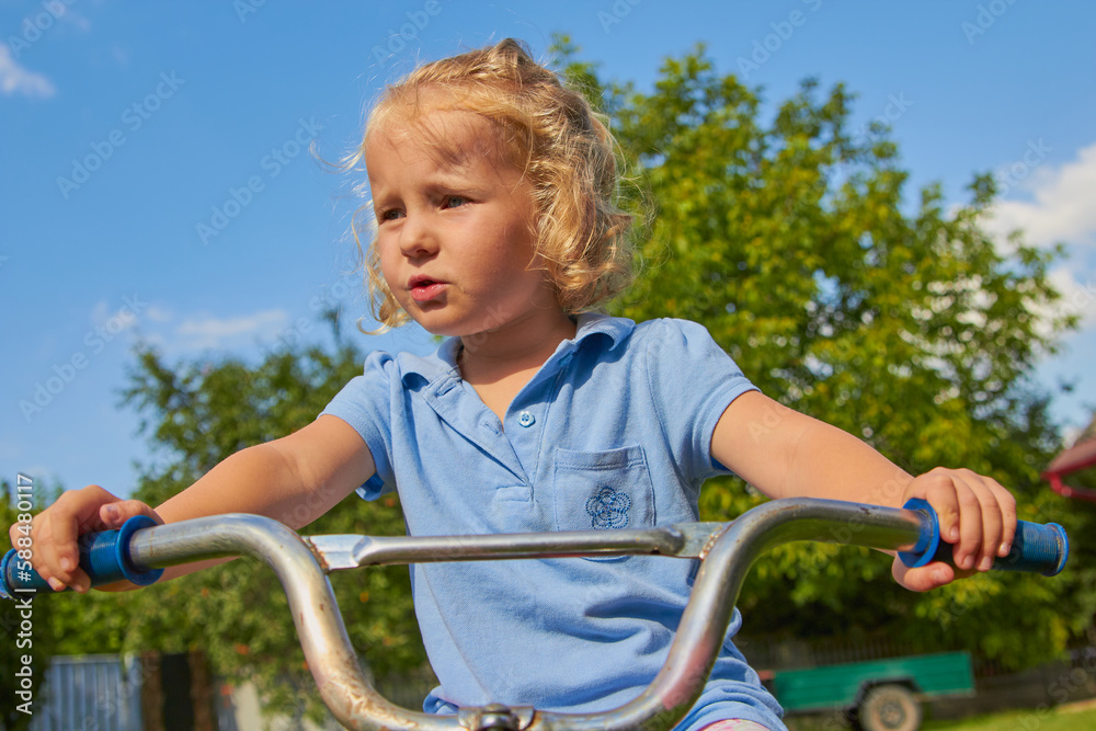 Obraz premium little girl driving a bicycle,a child holds the handlebars of a bicycle at sunset