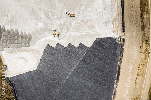 Aerial view of remediation work on a terrain with mining waste fillings, where working machinery and high-density geomembrane cover can be seen. photo