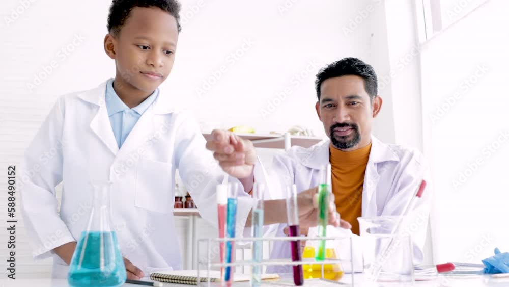 Teacher in white gown and student scientists making experiment in lab, teaching and guiding in his elementary school in science class. Happy african boy learning in chemistry class with professional Teacher in white gown and student scientists making experiment in lab, teaching and guiding in his elementary school in science class. Happy african boy learning in chemistry class with professional
