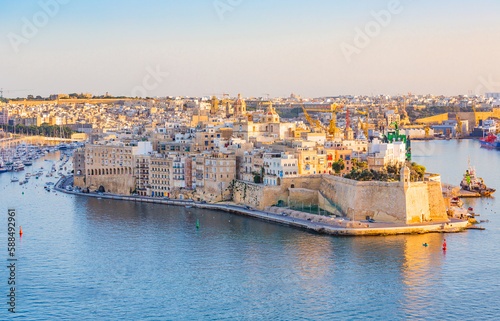This stunning photograph captures the three historic cities of Malta - Vittoriosa, Senglea, and Cospicua - basking in the warm glow of a golden sunset. Taken from the vantage point of La Valeta, the c photo