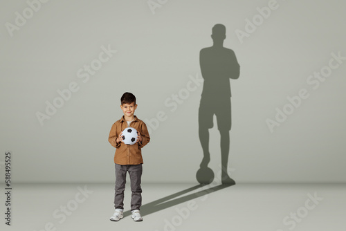 Happy caucasian 6 years old little kid in casual with soccer ball and shadow of adult soccer player