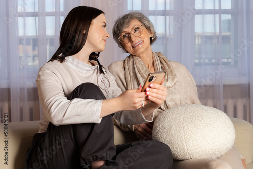 A young girl is explaining to an elderly woman how to use a phone. The granddaughter is showing her phone to her grandmother. a family pastime, helping and respecting the elderly.