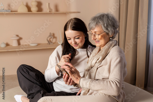 A young girl is explaining to an elderly woman how to use a phone. The granddaughter is showing her phone to her grandmother. a family pastime, helping and respecting the elderly.