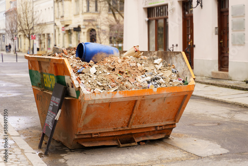 The yellow metal bin is filled with building debris and is ready to be collected from the street © Dzmitry