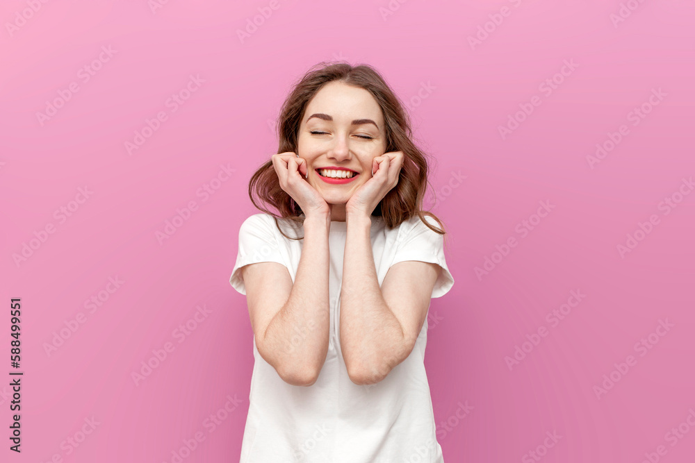 young modest loving woman dreams and rejoices with her eyes closed on pink isolated background young modest loving woman dreams and rejoices with her eyes closed on pink isolated background