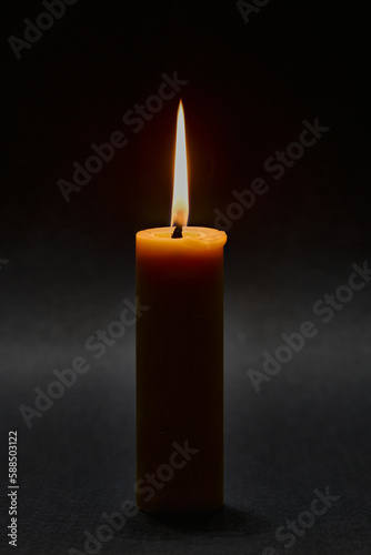 Woskowa świeca na czarnym tle. Płomień świecy rozświetla mrok.