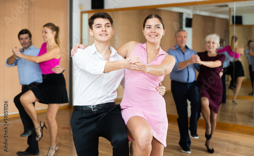 Cheerful young guy and girl practicing ballroom dances in ballroom