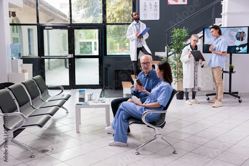 Physician nurse showing bottle of antibiotic to elderly man patient while explaining medication treatment during checkup visit examination in hospital waiting area. Health care service and concept © DC Studio