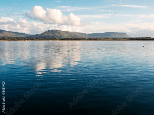 Benbulben mountain and blue water surface of Atlantic ocean with reflection of blue cloudy sky. Irish nature. County Sligo, Ireland. Popular tourist attraction. Stunning scenery.