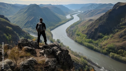 A person standing on a mountain peak with a view of a valley and a river below. Generative AI © Наталья Евтехова