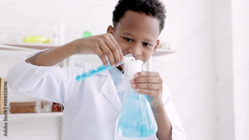 African student in white coat mixing chemical liquid in glass tube by using glass flask full of smoke, elementary schoolboy in science class acting thoughtful, kids scientist education concept African student in white coat mixing chemical liquid in glass tube by using glass flask full of smoke, elementary schoolboy in science class acting thoughtful, kids scientist education concept
