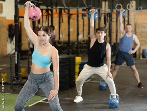 Sportive strong young female in activewear swinging kettlebell during group exercise class in health center indoors