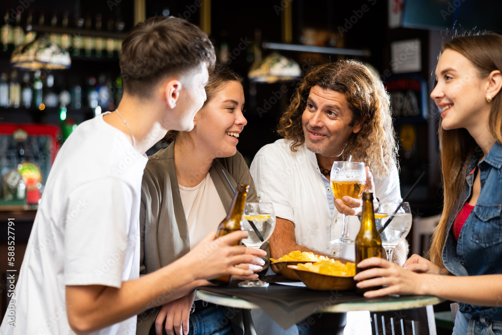 Group of friends standing at table in bar, drinking beer and having conversation.