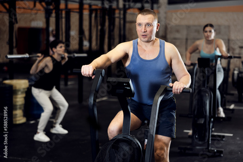 Portrait of concentrated adult man doing cardio training, cycling on stationary bike in gym. Sport and fitness concept..