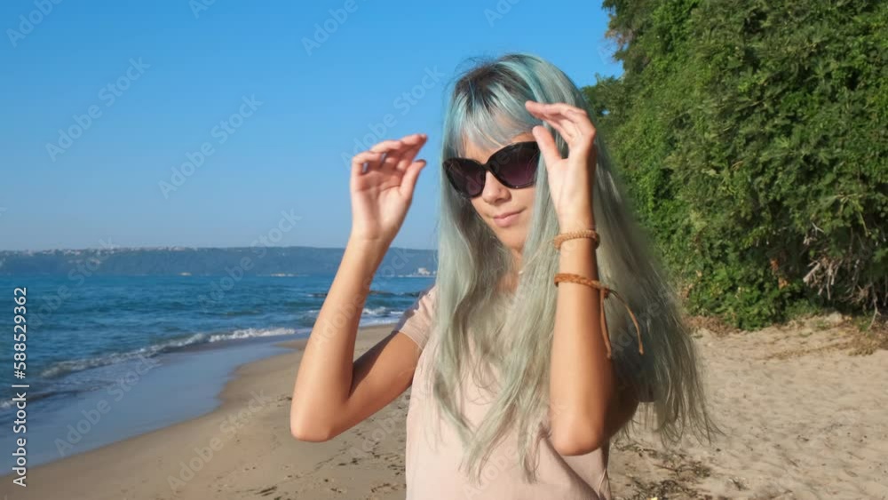 Girl in sun with wristband. A smiling young girl with blue hair wearing nice wristband during her sea stroll on the beach. A concept of lonely promenade during tropical vacation. Girl in sun with wristband. A smiling young girl with blue hair wearing nice wristband during her sea stroll on the beach. A concept of lonely promenade during tropical vacation.