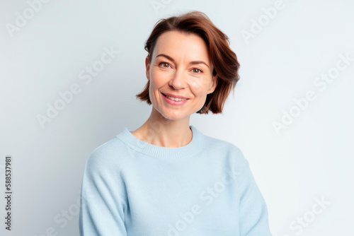Smiling happy woman in her 40s wearing sky blue sweater with short brown hair on white background.