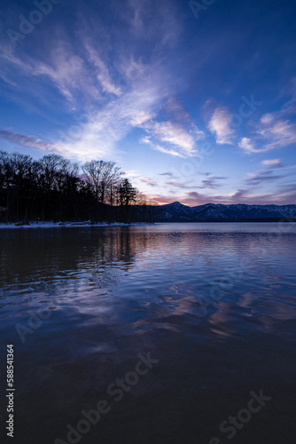 Fototapeta Naklejka Na Ścianę i Meble -  湖畔の森の木々と山と空を水面に反射する夜明けの湖。日本の北海道の屈斜路湖。