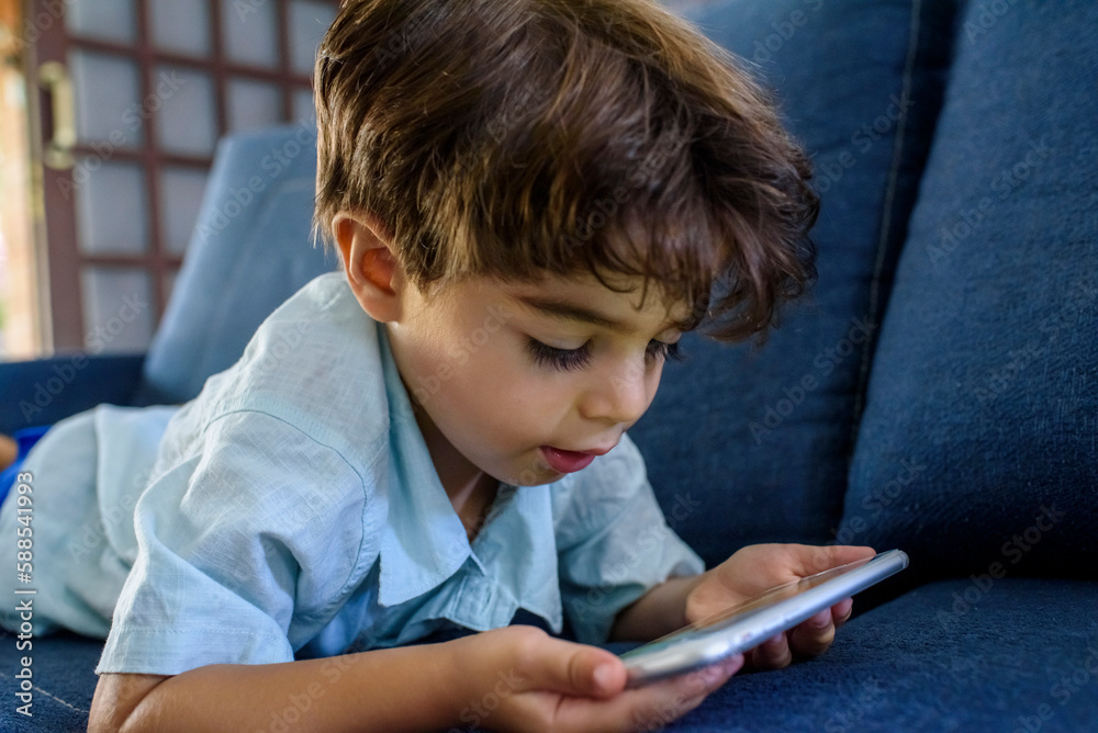 Boy about four years old watching video on mobile phone attentively on sofa at home. Boy about four years old watching video on mobile phone attentively on sofa at home.