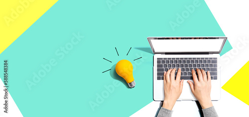 Person using a laptop computer and a light bulb - Flat lay photo